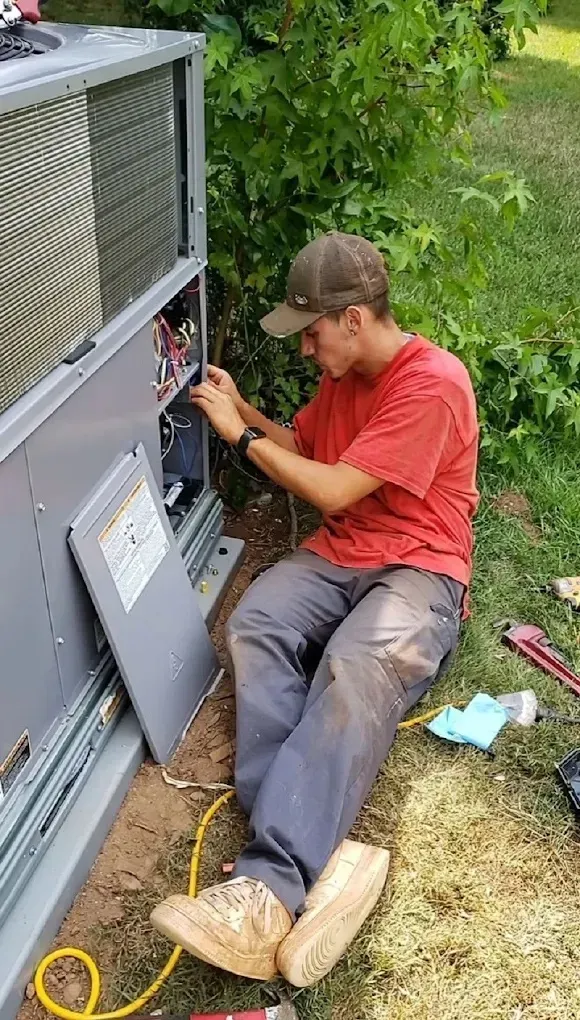 HVAC Blog 2 Technician repairing an air conditioning unit outdoors, surrounded by greenery.